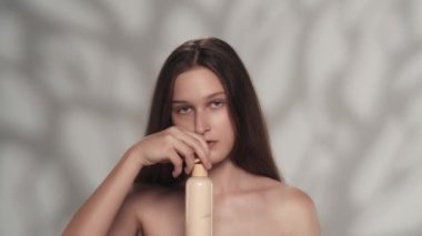 Çekici beyaz bir modelin portresi. Bir kızın elinde bir şişe vücut losyonu tutarken kameraya bakarken yakın plan fotoğrafı. Vücuduna nemlendirici krem sürüyor. Güzellik bakım reklamı.