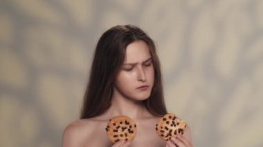 Çekici esmer modelin portresi. Elinde iki kurabiye olan ve hangisini deneyeceğine karar veren bir kızı yakından çek. Bir kurabiye seçiyor, ısırıyor ve tadını çıkarıyor. Diyet reklam kavramı.