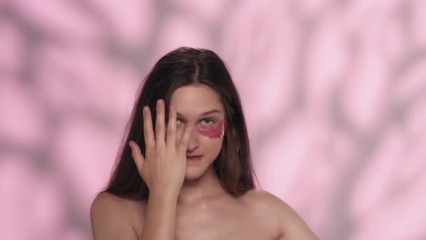 一个美丽的高加索女性模特的肖像 一个女孩的近照 眼皮底下有粉色眼罩 在镜头前笑着鬼鬼祟祟地捂着脸眼科护肤广告概念 — 图库视频影像