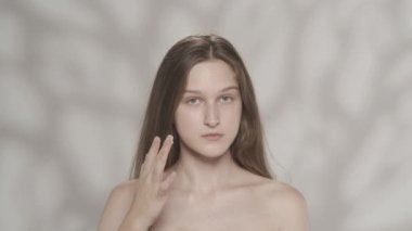 Beyaz kadın modelin çekici portresi. Bir kızın kameraya bakıp yanaklarına nemlendirici krem sürdüğü yakın çekim. Cilt bakımı reklam konsepti. HDR BT2020 HLG Malzemesi