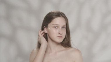 Beyaz kadın modelin çekici portresi. Yüzünde krem olan bir kızı yakından çek. Parmaklarıyla krem sürüyor ve kameraya bakıyor. Güzellik derisi reklam konsepti. HDR