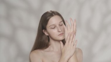 Beyaz tenli esmer modelin portresi. Bir kızın kameraya bakıp eline nemlendirici krem sürdüğü yakın plan bir fotoğraf. Bakım reklamları konsepti. HDR BT2020 HLG Malzemesi.