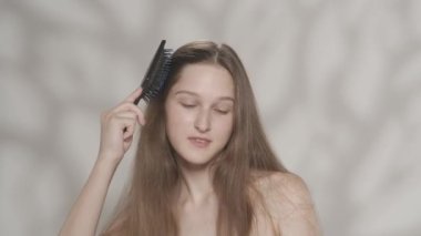 Mükemmel ciltli ve doğal makyajlı güzel bir kadın modelin portresi. Uzun ipek saçlarını tarayan ve kameraya bakan bir kızın yakın çekim görüntüsü. Saç bakım reklamı konsepti. HDR BT2020 HLG