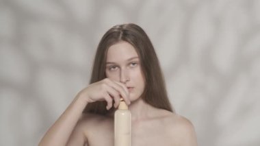 Çekici beyaz bir modelin portresi. Bir kızın elinde bir şişe vücut losyonu tutarken kameraya bakarken yakın plan fotoğrafı. Vücuduna nemlendirici krem sürüyor. Güzellik bakım reklamı.