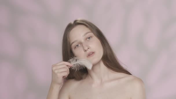 一个年轻漂亮姑娘的画像 模特拿着羽毛在脸上 头发上和肩膀上玩耍的特写镜头 被粉红色的背景隔离了恐怖广告的概念 Hdr — 图库视频影像