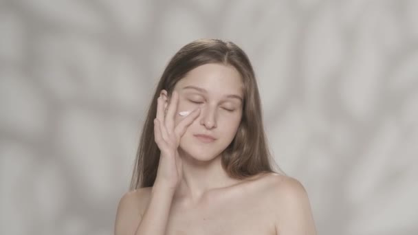 魅力的な白人モデルの肖像画 カメラを見て 顔と頬のエリアに保湿クリームを塗った少女のショットを閉じます 美容スキンケア広告コンセプト Hdr Bt2020について — ストック動画