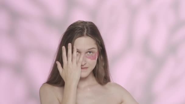 一个美丽的高加索女性模特的肖像 一个女孩的近照 眼皮底下有粉色眼罩 在镜头前笑着鬼鬼祟祟地捂着脸眼部护肤广告的概念 Hdr — 图库视频影像