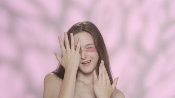 一个美丽的高加索模型的肖像 一个女孩的近照 眼皮底下有粉色眼斑 开玩笑地掩藏她的脸 对着相机笑 眼科护肤广告概念 — 图库视频影像