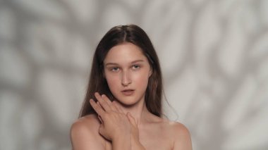 Beyaz tenli esmer modelin portresi. Makyajlı bir kızın kameraya bakıp ellerinin pürüzsüz tenine dokunuşunu yakından çek. Bakım reklamları konsepti.