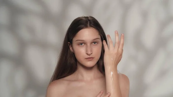 控えめな白人ブルネットモデルの肖像画 カメラを見ている化粧をした女性のクローズアップショットと 彼女の手に保湿クリームを塗ります ハンドケア広告コンセプト — ストック写真