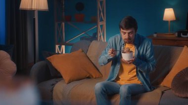 Bir adam oturma odasındaki kanepede otururken açgözlülükle dondurma yiyor.