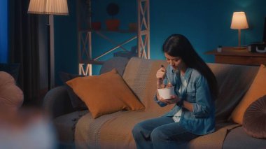 Asyalı kadın oturma odasındaki kanepede otururken kovadan çikolatalı dondurma yemekten hoşlanır.