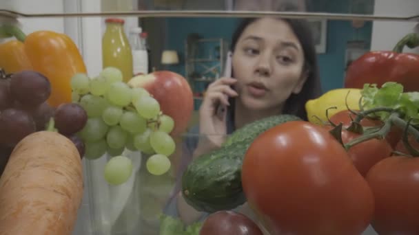 Een Aziatische Vrouw Staat Naast Een Open Koelkast Met Een — Stockvideo