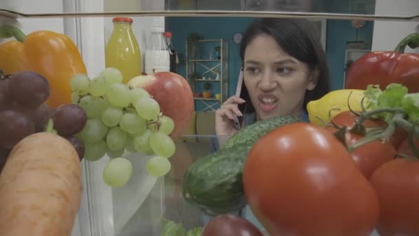 Ασιάτισσα Γυναίκα Μιλάει Στο Smartphone Ενώ Στέκεται Κοντά Ανοιχτό Ψυγείο — Αρχείο Βίντεο