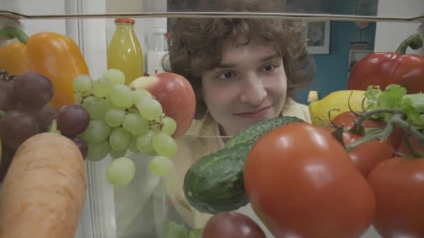 Ein Junger Mann Untersucht Einen Kühlschrank Der Mit Gesunden Produkten — Stockvideo
