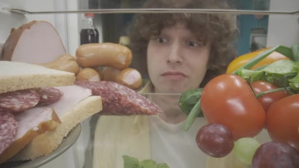 Egy Férfi Áll Egy Nyitott Hűtőben Egészséges Egészségtelen Ételekkel Zavarodott — Stock videók