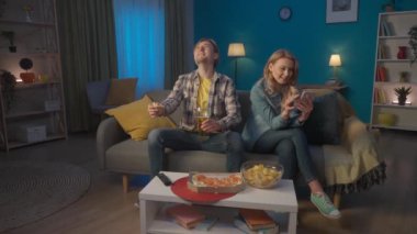 Bir bardak birası ve pizzası olan bir adam, maç seyrediyor, kaybettiği için üzgün. Kadın elinde telefonun yanında oturuyor, adamı görmezden geliyor, kayıtsızca onu dinliyor. Yavaş çekim