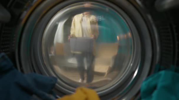 身穿便衣 提着洗衣篮的成年妇女打开洗衣机的门 拿出干净的衣服 她嗅着新鲜的衣服笑了 从洗衣机内观看 — 图库视频影像