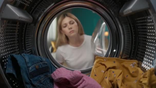 身穿便衣 提着洗衣篮的成年妇女打开洗衣机的门 拿出干净的童装 她看上去很高兴 对着摄像机笑了 从洗衣机内观看 — 图库视频影像