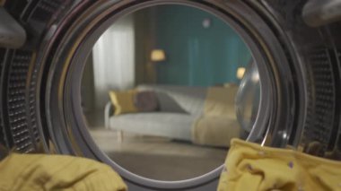 Çamaşır makinesi varilin içinde renkli giysilerle dolu ve kapısı açık. Çamaşır günlük rutin konsept. Ev ilanı. Çamaşır makinesinin içinden boş bir oturma odasına bak. HDR