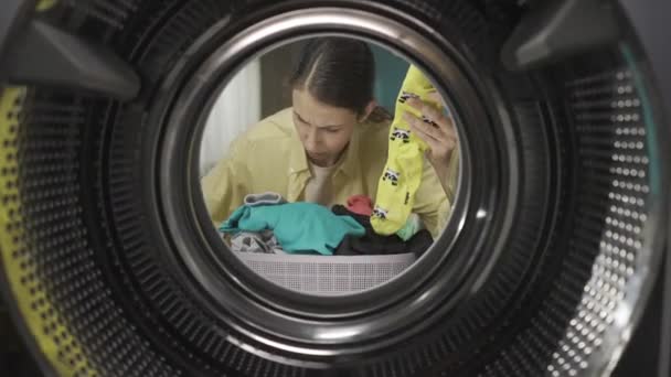 穿着休闲装的年轻女人拿着一个装满干净衣服的洗衣篮 她挑了两双不同颜色的袜子 试图找到它们的搭配 从洗衣机的内部观看 Hdr Bt2020 — 图库视频影像
