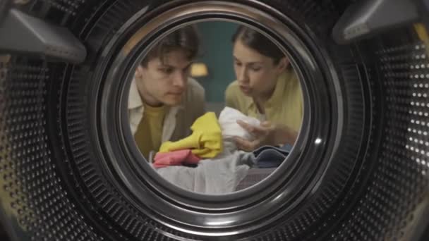 年轻夫妇在洗衣服 女人向她的男人解释和展示如何洗衣服和使用洗衣机 夫妻一起做家务活很开心 从空洗衣机的内部观看 Hdr — 图库视频影像
