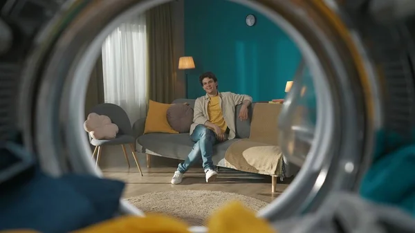 美しいリビングルームのソファーに座ってカジュアルな服を着た大人の男性は カメラを見ながら微笑んでいます 洗濯機の中からの眺め — ストック写真