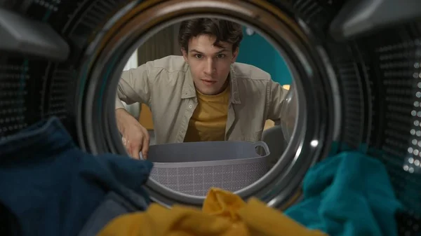 洗濯バスケット付きのカジュアルな服を着た大人の男性が洗濯機のドアを開け 新鮮な服を取り出します 洗濯機の中からの眺め — ストック写真