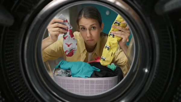 一个穿着休闲装的年轻成年女子的画像 手里拿着不同的袜子 看上去很困惑 从洗衣机内观看 — 图库照片