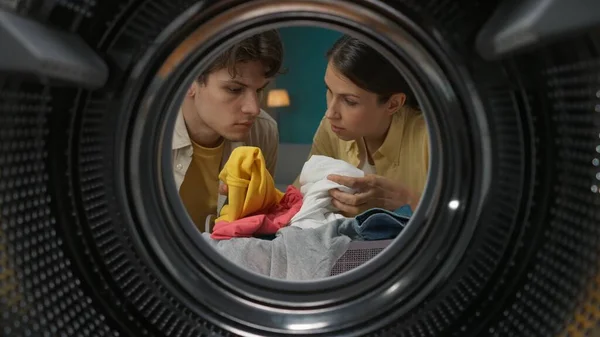 年轻夫妇在洗衣服 女人向她的男人解释和展示如何洗衣服和使用洗衣机 从空洗衣机的内部查看 — 图库照片