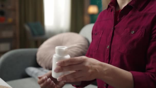 一个金发女郎坐在沙发上 手里拿着药瓶 手里拿着一堆药丸的特写镜头 家庭医学的概念 卫生保健广告 慢动作 — 图库视频影像