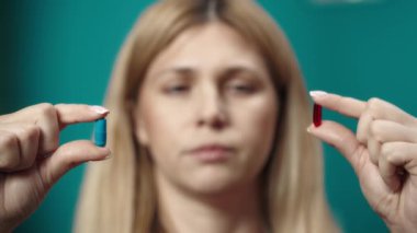 Kadın modelin elinde mavi ve kırmızı kapsülleri tutarken ve hangisini seçeceğine karar verirken yakın çekim. Mavi olanı seçen ve gülümseyen bir kadın. Ev hekimliği konsepti. Sağlık hizmeti reklamı. Yavaş