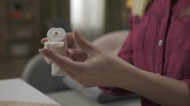 Kanepede oturan yetişkin bir kadın modelin, tüpten bir merhem sıkarken ve bilek bölgesine sürerken yakın plan fotoğrafı. Artrit tedavisi. Ev hekimliği konsepti. Sağlık hizmetleri reklamı