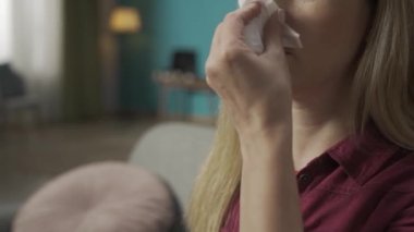 Sarışın bir kadının kanepede oturup burnunu kağıt mendille silerken yakın plan çekimleri. Burnuna burun spreyi sıkarak. Rhinitis tedavisi. Ev hekimliği konsepti. Sağlık hizmeti reklamı. HDR