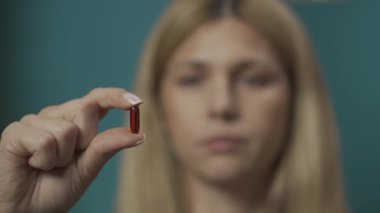 Kafkasyalı sarışın kadın portresi. Kadın modelin elinde kırmızı bir kapsül hapı tutarken yakın plan fotoğrafı. Kameraya gösteriyor. Ev hekimliği konsepti. Sağlık hizmeti reklamı. Yavaş çekim HDR