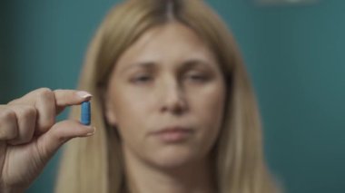 Kadın modelin elinde mavi ve kırmızı kapsülleri tutarken ve hangisini seçeceğine karar verirken yakın çekim. Kadın kırmızıya bakıyor ve olumsuz bir şekilde başını sallıyor. Ev hekimliği konsepti. Yavaş çekim HDR