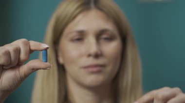 Kadın modelin mavi ve kırmızı kapsülleri tutarken yakın plan çekimleri. Kadın mavi hapı seçer ve kırmızı hapı alır. Ev hekimliği konsepti. Sağlık hizmeti reklamı. Yavaş çekim