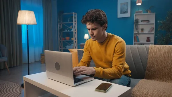 남자는 저녁에 거실에서 소파에 앉아있는 노트북에서 작동합니다 이메일 온라인 — 스톡 사진