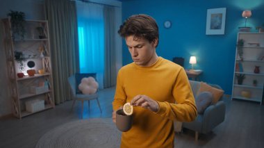 Oturma odasında bir elinde bir fincan çay, diğerinde bir dilim limon olan bir adam duruyor. Bir adam limonlu sıcak çay içecek. Ev hekimi konsepti