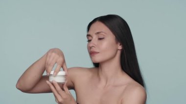 Cilt bakımı için krem. Bir seminer kadını bir krem kavanozunun kapağını açar ve aromasını içine çeker. Stüdyoda elinde kremayla mavi arka planda olan bir kadın. Güzellik kavramı