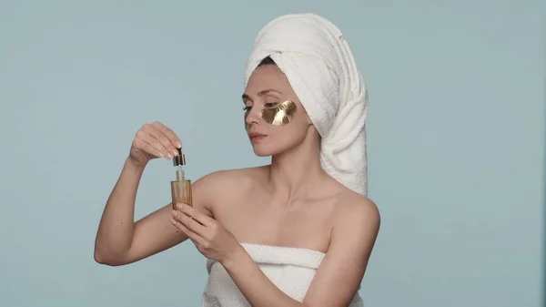 一名妇女在淋浴后裹上浴巾 眼皮底下闪烁着金色斑斑 在淋浴后进行美容美发 一个女人手里拿着一瓶精油和一支长笛 — 图库照片
