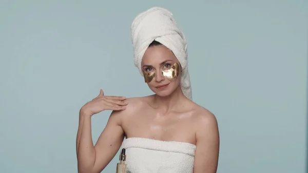 一名妇女在淋浴后裹上浴巾 眼皮底下闪烁着金色斑斑 在淋浴后进行美容美发 一个女人手里拿着一瓶香精油 手里拿着一支长笛 — 图库照片