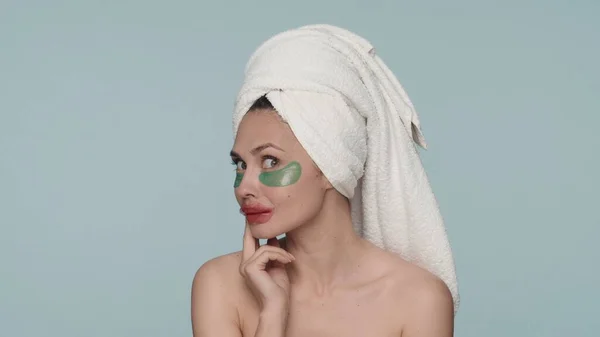 一个头戴毛巾 头戴蓝色背景的神童女人的画像 一个女人在淋浴后做化妆品 在她的眼睛和嘴唇上涂上水胶补丁 — 图库照片