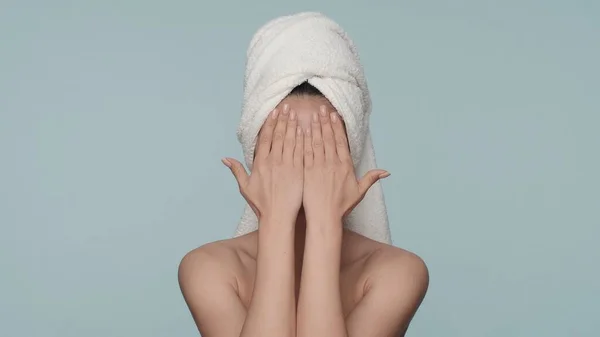 一位皮肤有问题的妇女在工作室里用双手捂住脸 她的背景是蓝色的 一个头戴毛巾的神童女人因为皮肤不完美而感到没有安全感 — 图库照片