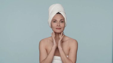 Stüdyoda banyo havlularına sarılı mavi arka planda bir kadının portresi. Bir kadın, duştan sonra pürüzsüz ve temiz cildinin tadını çıkarır. Güzellik konsepti, kozmetoloji, cilt bakımı