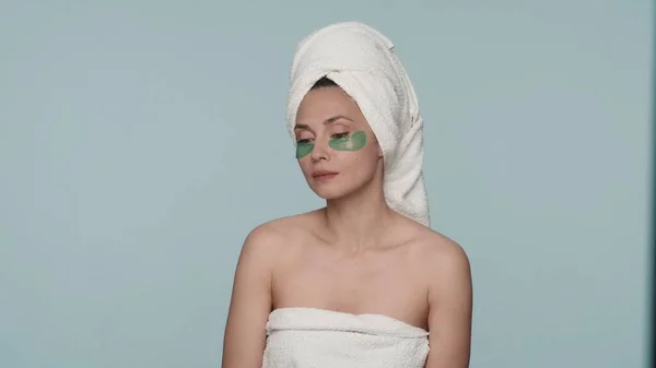 穿着浴巾的女人在蓝色背景的淋浴后裹在浴巾里 一个有着绿色水凝胶斑块的女人的画像 紧闭双眼 护肤的概念 — 图库照片