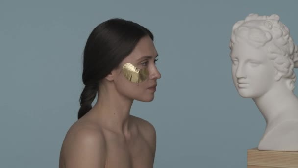 Woman Golden Patches Her Eyes Looks Female Plaster Bust Front — Stock Video