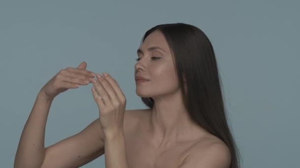 女性が適用され 青い背景に彼女の手の皮にクリームをこすります セミナーの女性は彼女の顔に触れ 彼女の手の柔らかさを楽しみます 化粧品 ハンドスキンのコンセプト — ストック動画
