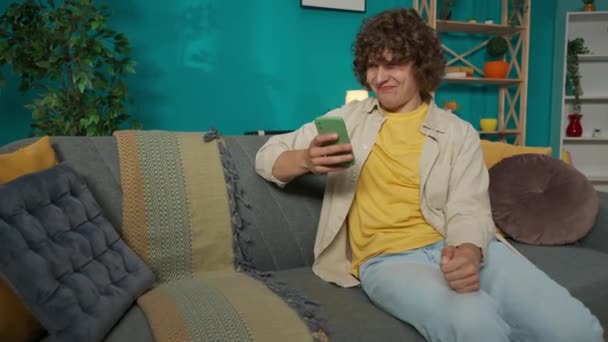 Oturma Odasındaki Kanepede Günlük Giysiler Içinde Oturan Genç Bir Erkek — Stok video