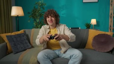 Oturma odasındaki kanepede oturan genç bir erkeğin portresi. Oyun konsolu olan bir adam joystick ile oyun oynuyor. Maçı kaybettiği için üzülüyor ve üzülüyor. Ev video oyunları reklamı